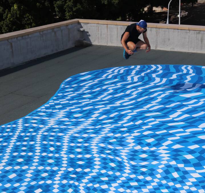 BOMBS AWAY: Artist Lucas Grogan tests the 'waters' of his whimsical rooftop mural, painted atop a 'secret' city location. Picture: Supplied
