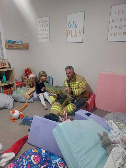 Doyalson Station Officer Dirk Ziekenheiner reads one of local girl Mia's stories after extinguishing a fire in the family home at Blue Haven. Pictures supplied