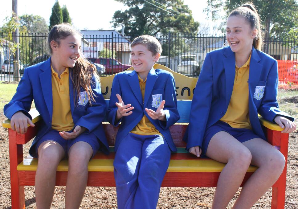 Year six Cardiff Public School students Brewannin Murray, Jack Bateman and Olivia Dugan test the new buddy bench, donated to the school by the Cardiff District Men's Shed.