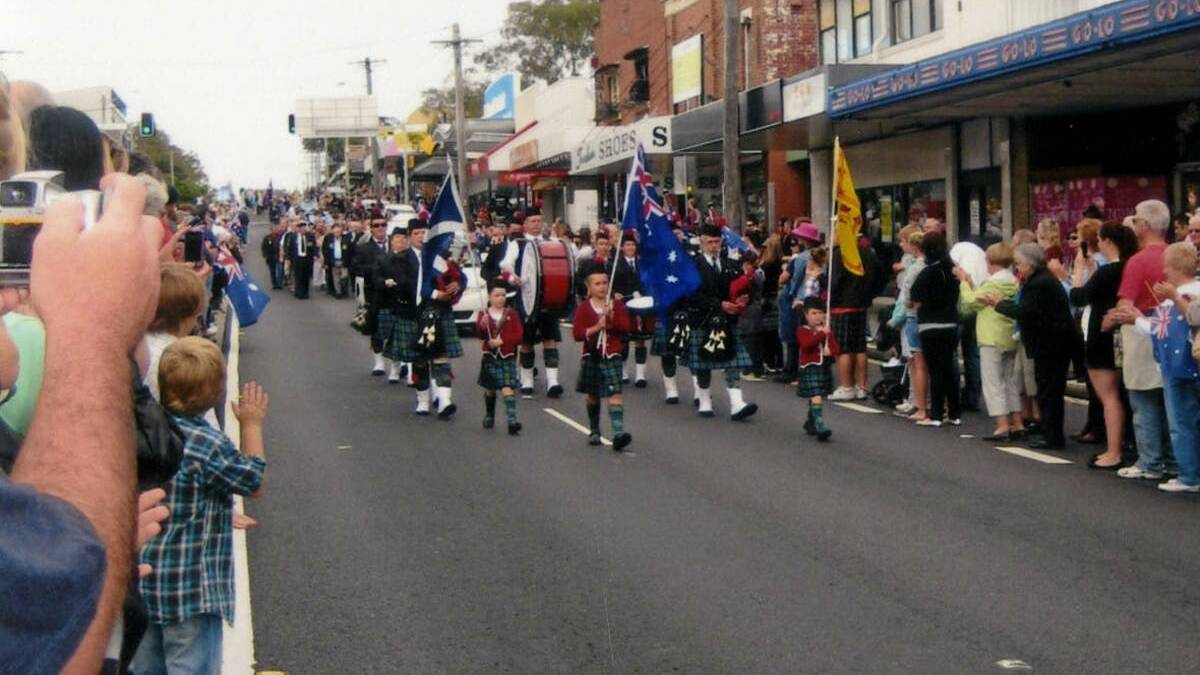 BANDING TOGETHER: Crowds line the Pacific Highway as the Clan McEwan Pipe Band performs at Belmont’s 2012 Anzac Day parade