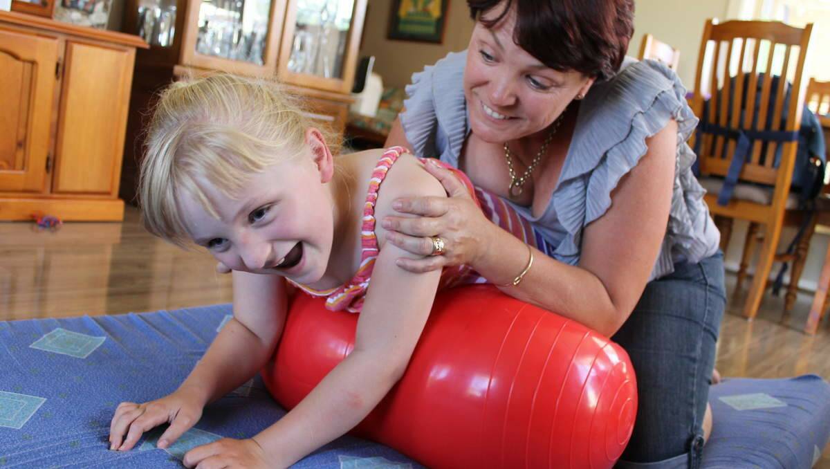 HOW THEY ROLL: Kobi Robbs, 7, being helped by her mum, Nicole, with her daily exercises on a therapy peanut ball. Photo by Mark Connors