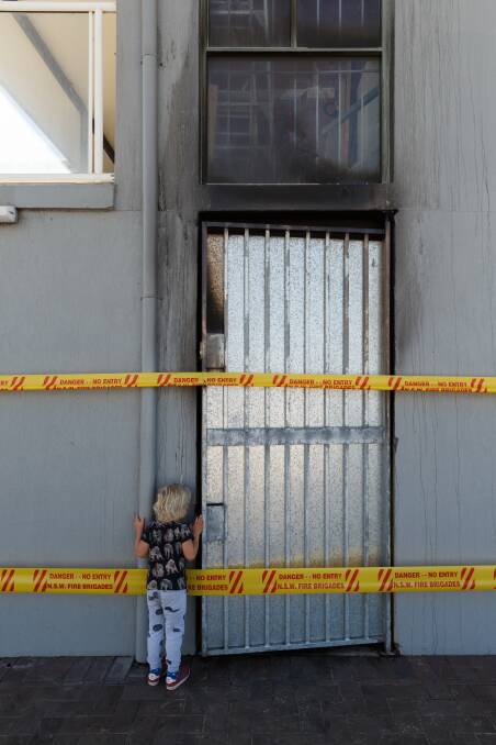 BLACKENED: Four-year-old Tex Ayre takes a peek through the door of the Redhead Beach Cafe, destroyed by fire on Saturday morning. Picture: Max Mason-Hubers 