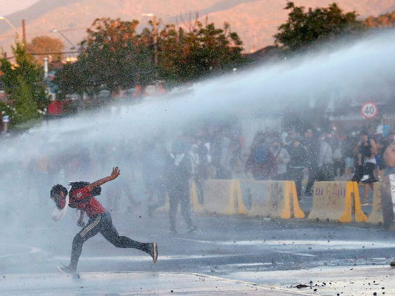 A protester runs from water cannon during a rally against Chile's government.